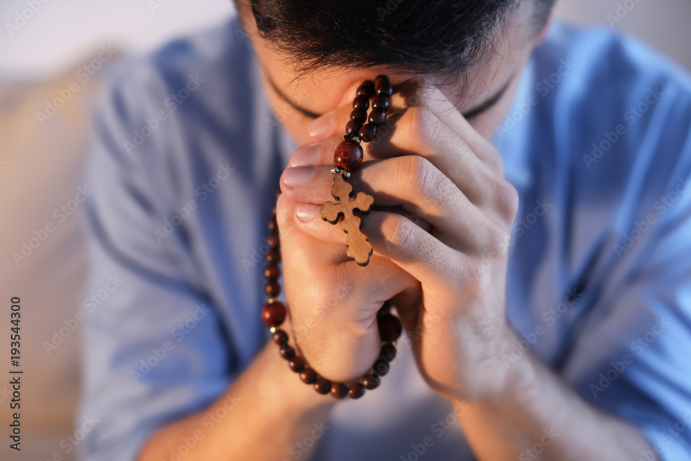 Obraz premium Religious young man with rosary beads praying at home, closeup