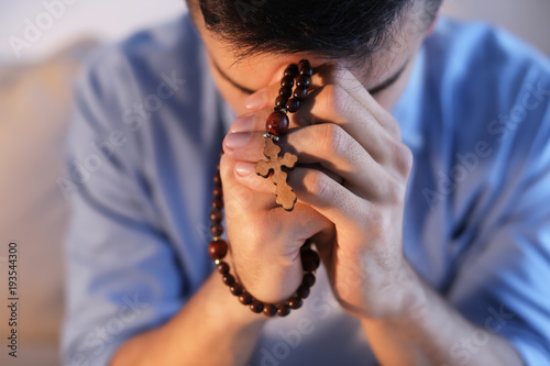 Fototapeta Religious young man with rosary beads praying at home, closeup