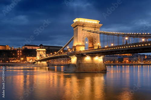 Chain bridge in Budapest under light beam through clouds at night