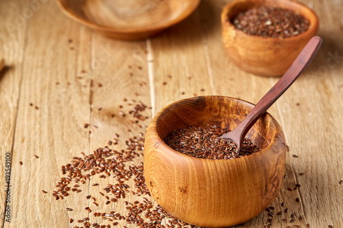 Flax seeds in wooden bowl and spoon on rustic wooden background, top view, shallow depth of field
