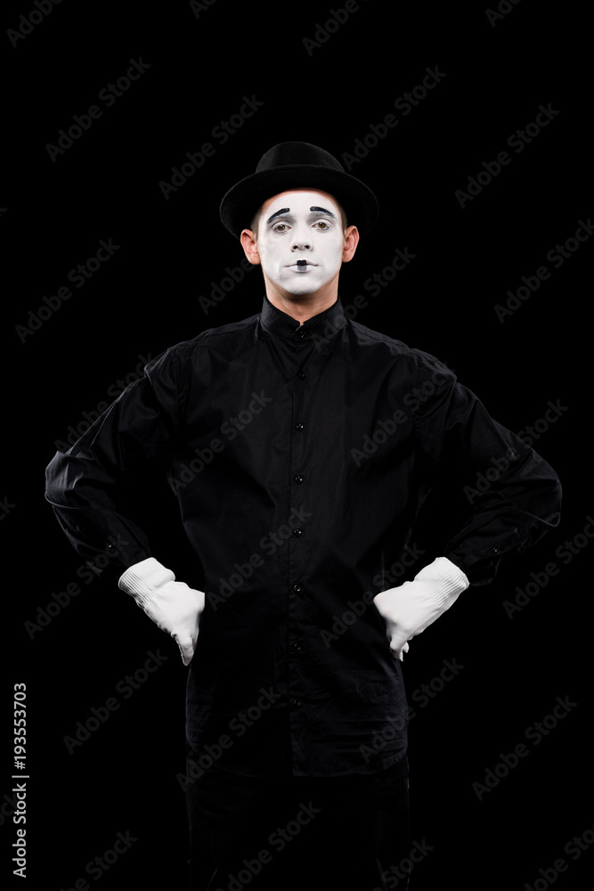 Obraz premium mime standing with hands akimbo and looking at camera isolated on black