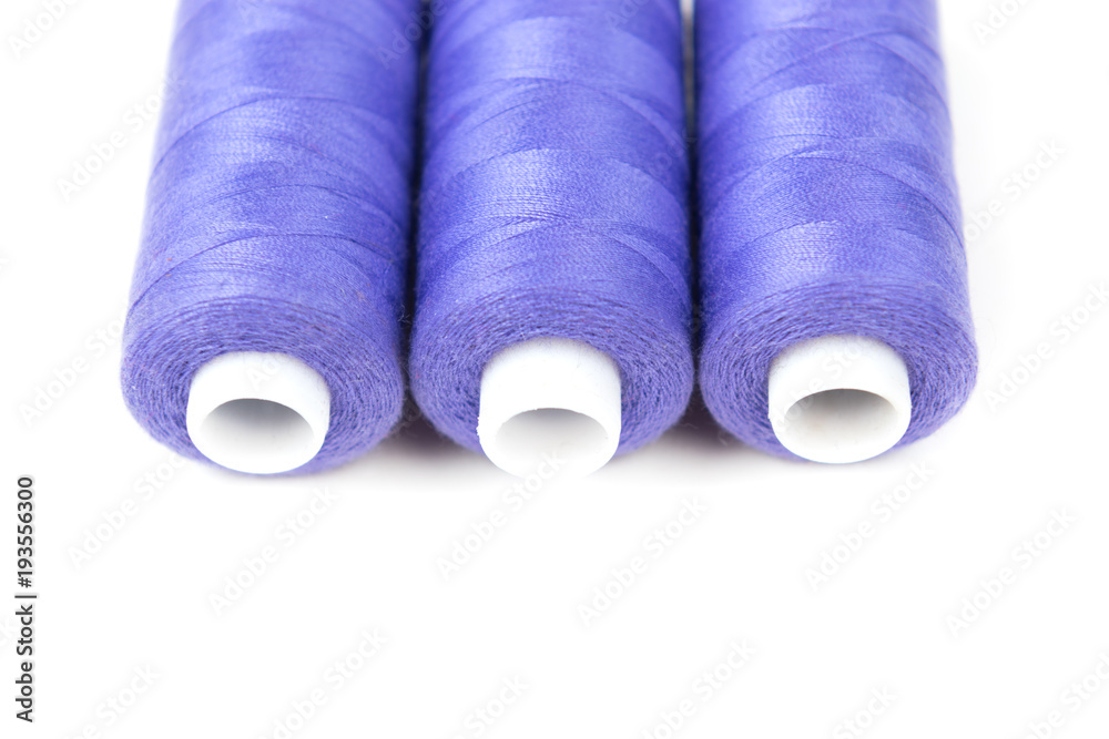 Three purple sewing threads on a white background, sewing accessories and supplies Three purple sewing threads on a white background, sewing accessories and supplies