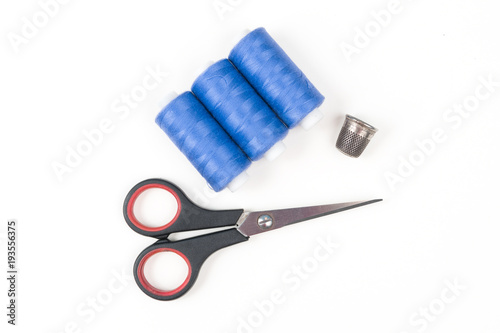 Blue sewing threads with black scissors and metal thimble on a white background