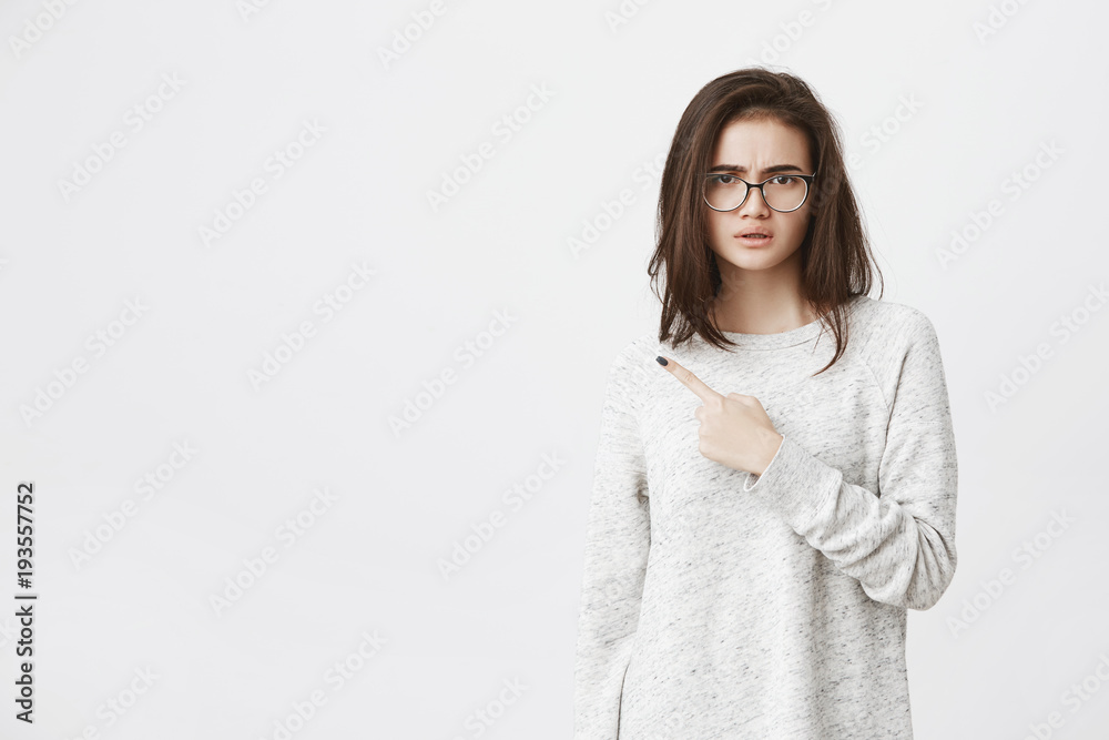 Portrait of young attractive model with angry and puzzled expression, pointing at upper left conner, over white background. Newcomer just heard her coworkers were discussing her. Portrait of young attractive model with angry and puzzled expression, pointing at upper left conner, over white background. Newcomer just heard her coworkers were discussing her.