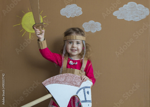 Young girl on stick horse. Handmade. Background of painted sun and white clouds