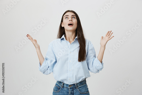 relieved and gladful young european female raising hands and looking up with opened mouth and satisfied expression, standing over gray background. Student is happy that lecture finally over