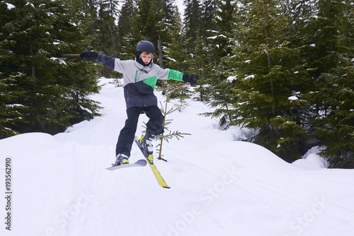 Little boy jumping on downhill skis in forest. Skiing between trees. Adrenaline sport in winter 