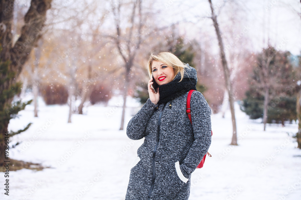 Beautiful hipster girl talking on the phone smiling and looking away outdoors in winter. Portrait of a modern girl with a mobile phone outdoors. Communication, space for text. Beautiful hipster girl talking on the phone smiling and looking away outdoors in winter. Portrait of a modern girl with a mobile phone outdoors. Communication, space for text.
