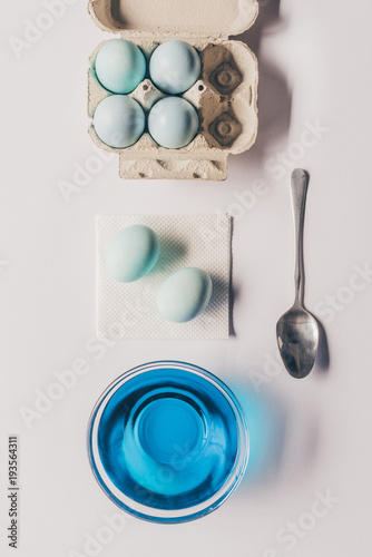 top view of glass with blue paint and chicken eggs in tray, easter concept