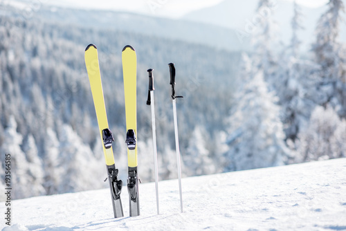 Skis with sticks on the snowy mountains with frozen forest on the background photo
