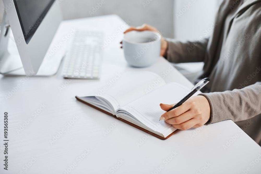 Schedule helps maintain my day. Cropped shot of woman working in front of computer, writing in notebook and drinking coffee. Businesswoman makes plan of her meeting during day Schedule helps maintain my day. Cropped shot of woman working in front of computer, writing in notebook and drinking coffee. Businesswoman makes plan of her meeting during day