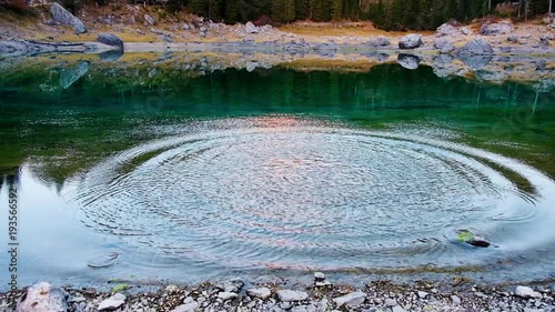 Stone falls into calm in Carezza lake water
