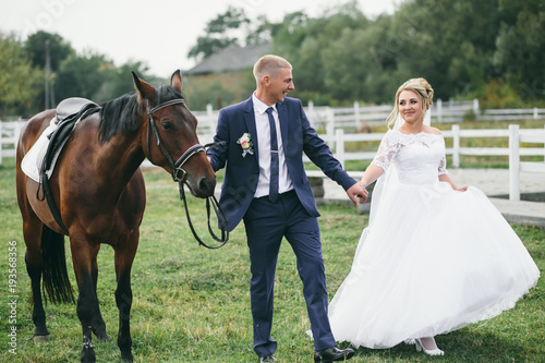 Gorgreous wedding couple poses on the green lawn with a horse