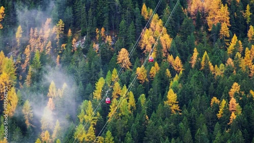 Forest trees with clouds and mist fog  and red ski lift in Dolomites