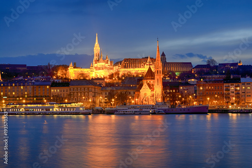 Illuminated St. Matthias church and Szil  gyi Dezs   cathedral across Danube river at night  Budapest