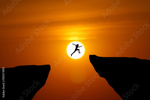 Man jump through the gap between hill.man jumping over cliff on sunset background,Business concept idea