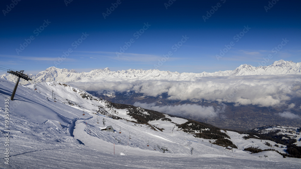 Chairlift at Italian ski area of Pila on snow covered Alps and pine trees during the winter with Mt. Blanc in France visible in background
