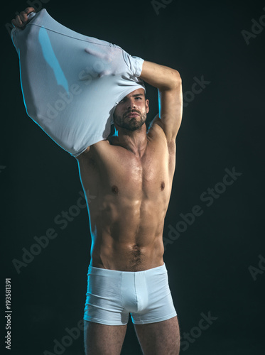 Torso of sexy man undressing white underwear, unshaven guy on dark  background, fashion model in studio. Sexy young man with muscular body  taking off t-shirt, showing bare muscular torso. Stock Photo