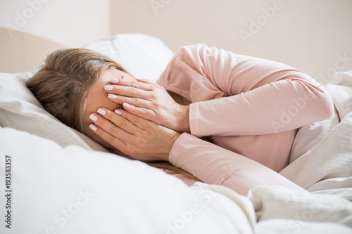 Sad woman covering her face while lying on a bed.