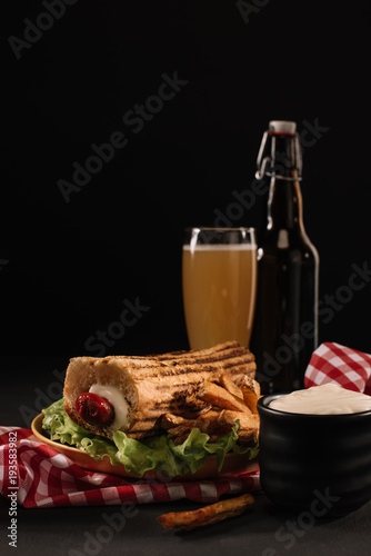 delicious french hot dog on plate with bottle and glass of beer isolated on black