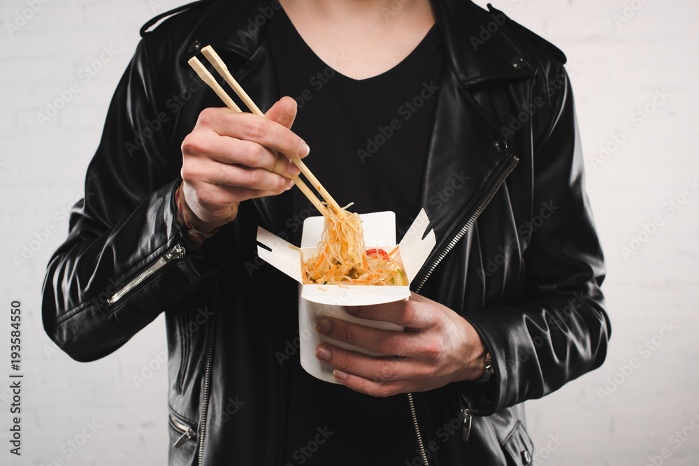 cropped shot of man in leather jacket holding noodles in box