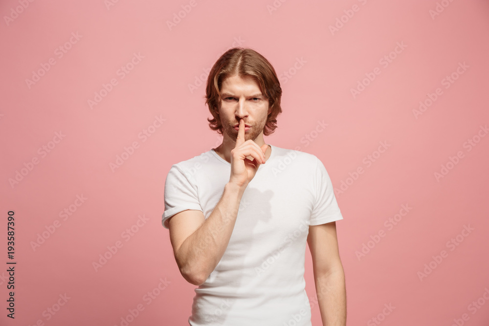 The young man whispering a secret behind her hand over pink background The young man whispering a secret behind her hand over pink background