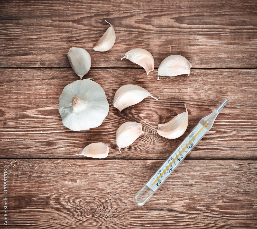 Garlic cloves and thermometer on a wooden table. Traditional medicine against colds.. Garlic cloves and thermometer on a wooden table. Traditional medicine against colds..