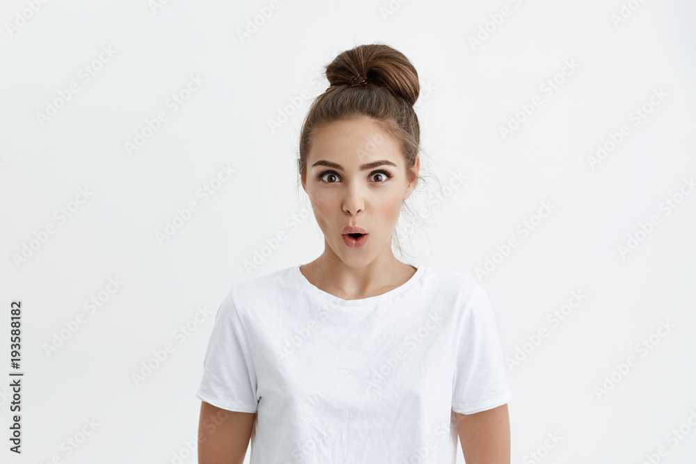 Portrait of attractive modern european model expressing surprise and excitement while glancing at camera with desire and standing with opened mouth over white background. Woman is shocked of huge sale Portrait of attractive modern european model expressing surprise and excitement while glancing at camera with desire and standing with opened mouth over white background. Woman is shocked of huge sale