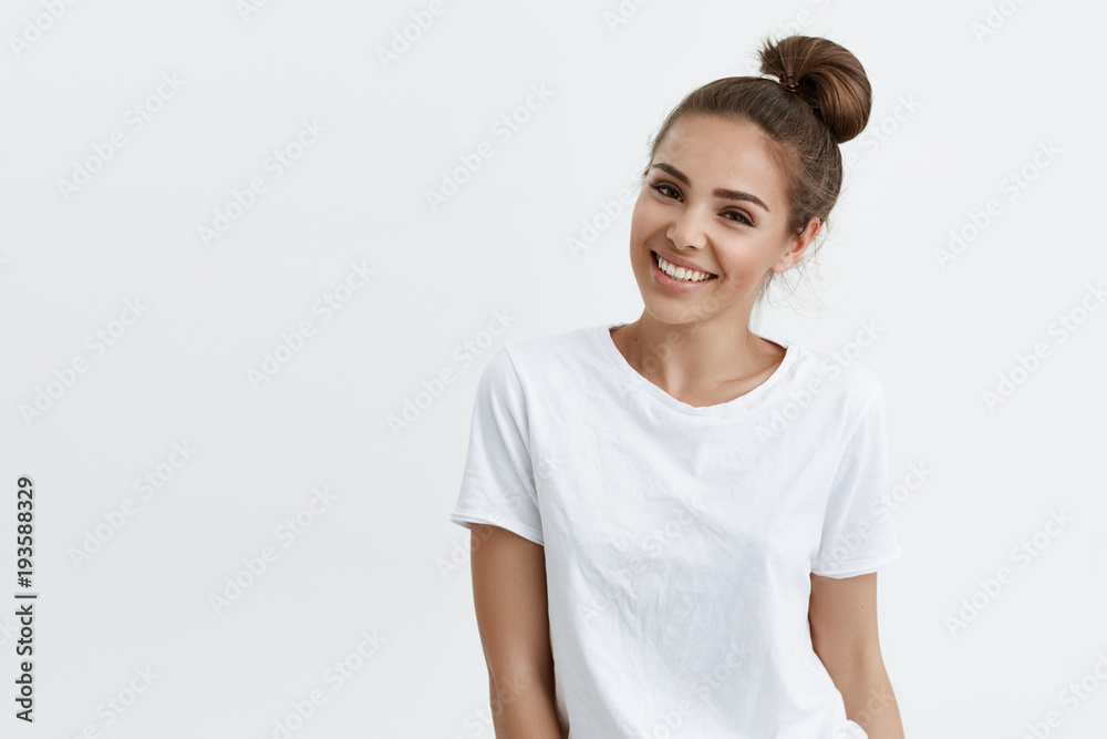 Positive slim european girl with bun hairstyle, smiling broadly while standing over white background, expressing confidence and sensuality. Makeup blogger records new video-tutorial Positive slim european girl with bun hairstyle, smiling broadly while standing over white background, expressing confidence and sensuality. Makeup blogger records new video-tutorial