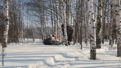 Man fast riding on mini snowmobile on deep snowdrifts in the forest and maneuvering between the trees photo