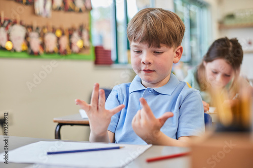 Schoolboy counting with fingers in classroom lesson at primary school photo