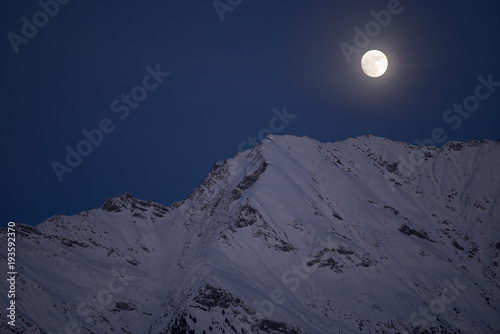 Vollmond über einem schneebedeckten Gipfel in den Schweizer Alpen