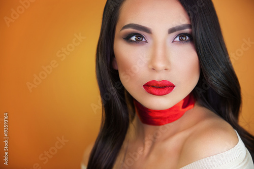 a beautiful girl with sensual bright red lips on an orange background, a red ribbon on her throat does not leave anyone indifferent, everyone looking into her brown eyes.