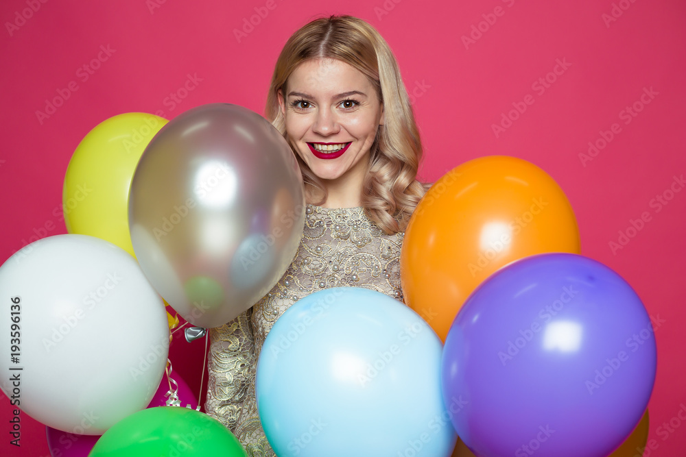 Obraz premium Birthday party. Concept of gifts and congratulations. Stylish young smiling beautiful blonde woman in evening dress on a pink background with large multi-colored helium balls.