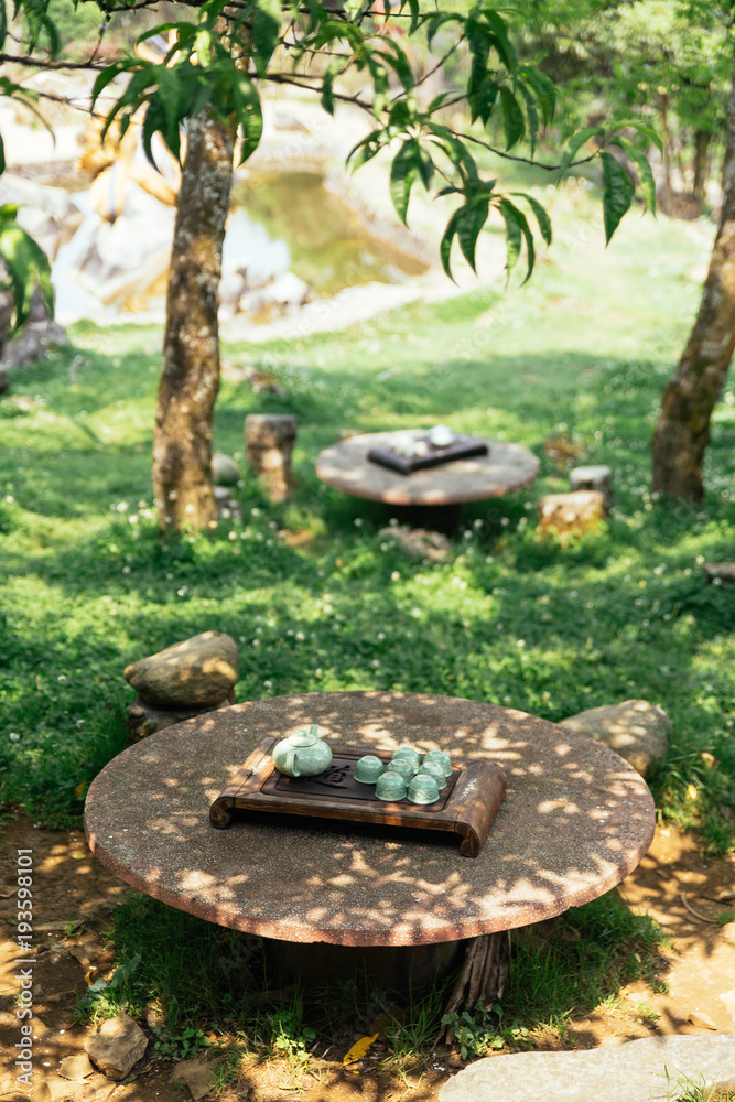 Light green ceramic tea set including pot, cups and plate on stone table under tree shadow at Ham Rong Mountain Park in Sa Pa, Vietnam. Light green ceramic tea set including pot, cups and plate on stone table under tree shadow at Ham Rong Mountain Park in Sa Pa, Vietnam.
