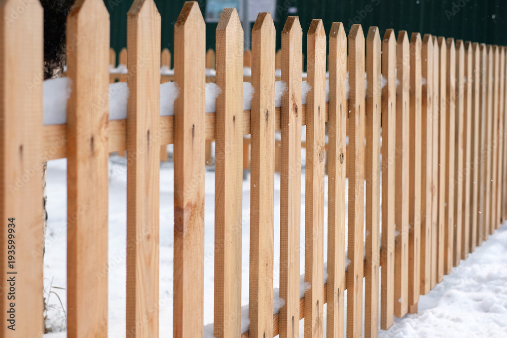 Wooden fence covered with snow around garden in winter time.