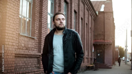 Wallpaper Mural Portrait of casual handsome Caucasian man. Confident young male in leather jacket walks by camera. Red brick wall 4K. Torontodigital.ca