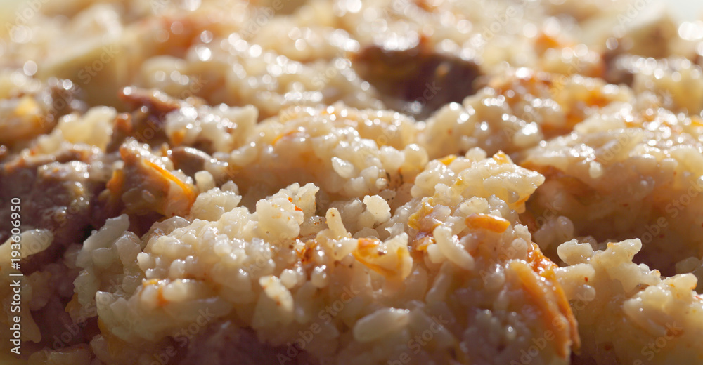 Pilaf from rice and meat with the addition of carrots and garlic. Prepared meal before consumption, fatty product close-up. Pilaf from rice and meat with the addition of carrots and garlic. Prepared meal before consumption, fatty product close-up.