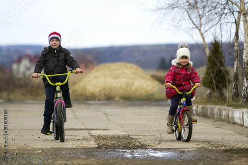 Two happy children boy and girl riding bicycles outdoors in cold weather