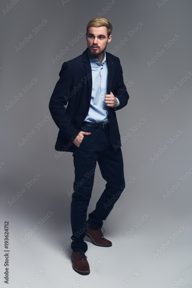 Stylish and professional. Fashionable entrepreneur holding lapel and put the other hand into the pocket in front of grey background. Stylish and professional. Fashionable entrepreneur holding lapel and put the other hand into the pocket in front of grey background.