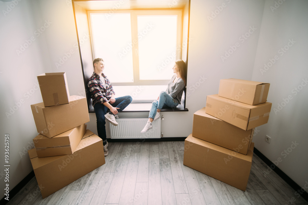 Fototapeta premium Portrait of young couple moving in new home sitting on windowsill and take a break.
