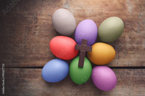 Wooden cross above the colored Easter eggs on wooden background
