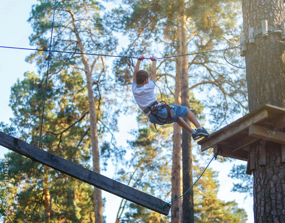 cute boy  climbs on a very risky treetops in rope adventure park in the summer