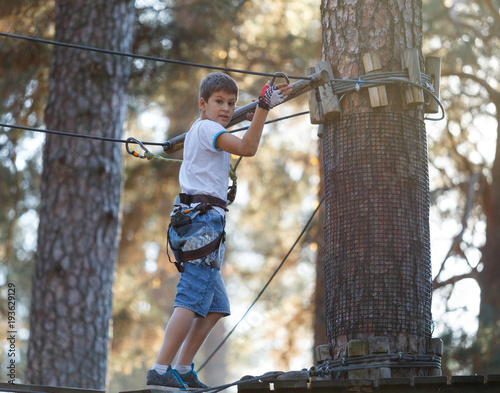cute boy goes on skateboard on the treetops in adventure rope park. he will cope with all challenges!