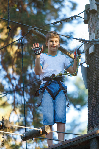 cute boy climbs on a very risky treetops in rope adventure park in the summer