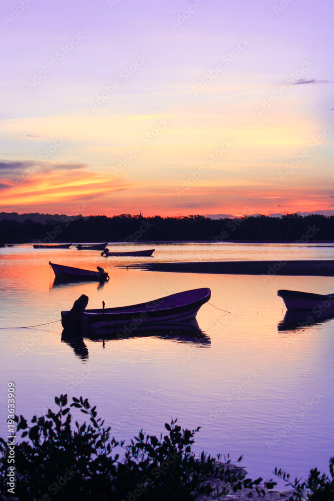 Vertically shot sunrise silhoutte of fishing boats with soft hues of purple and yellow.