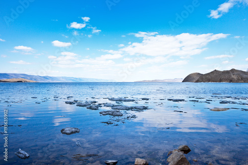 Ice drift on Lake Baikal. Spring day on the shore of the Kurkut Bay. The blue sky is reflected in the calm water