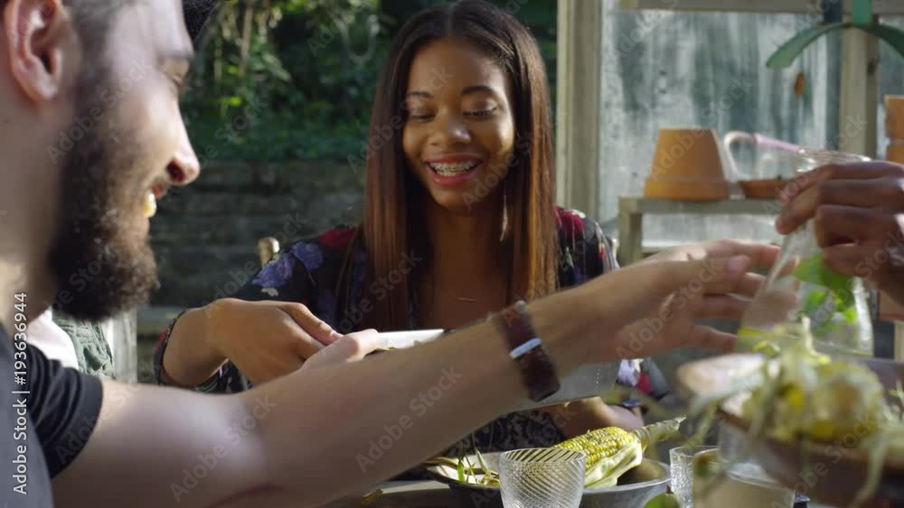 Young hip friends sharing food and drinks at table, slow motion