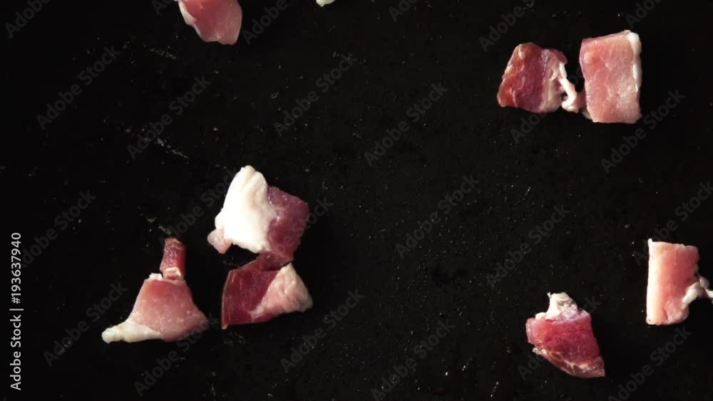 Bits of raw bacon drop on pan, close up