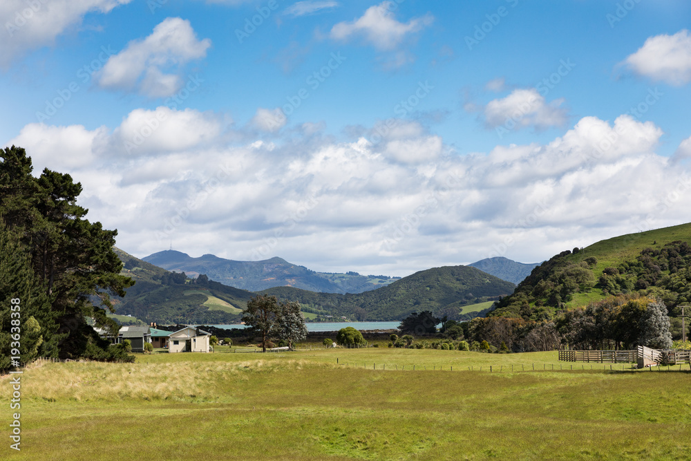 Farm house and paddock in rural Otago Peninsula, New Zealand, with coastline and mountains in distance